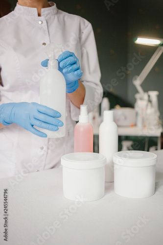 Close up of female hands in latex gloves with cosmetic and personal care products on table. Lady is wearing white lab coat. concept of professional beauty products © Kristina