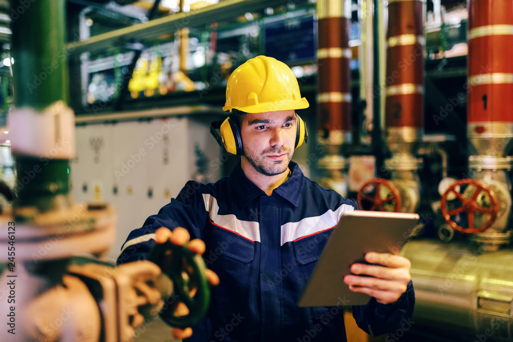 © Dusan Petkovic - Close up of worker waring protective suit while using tablet and tightening the valve while standing in heating plant. © Dusan Petkovic - Close up of worker waring protective suit while using tablet and tightening the valve while standing in heating plant.