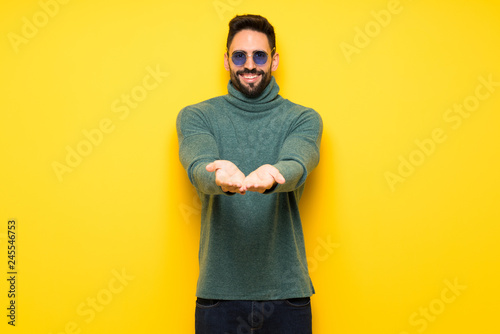Handsome man with sunglasses holding copyspace imaginary on the palm to insert an ad