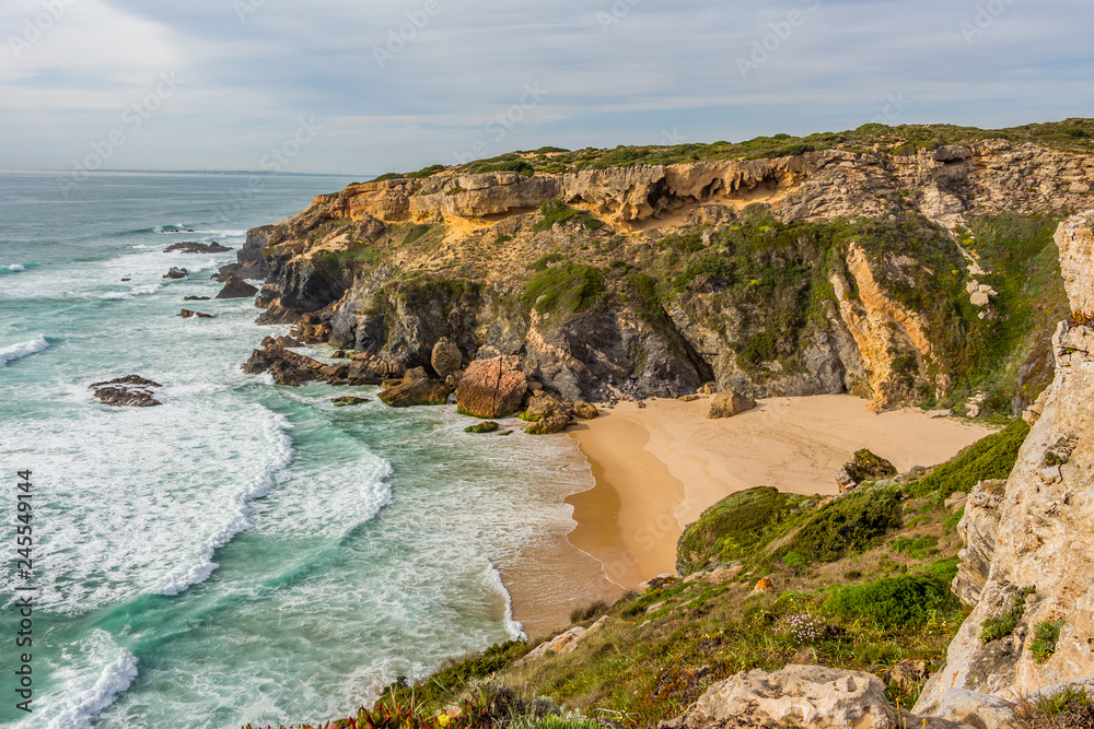 Wild sandy beach with cliffs on Atlantic Ocean coast, Rota Vicentina, Alentejo, Portugal. Small waves hitting the rocks.