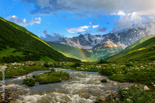 Rainbow over the rapid river and the snow-capped mountains. Georgia