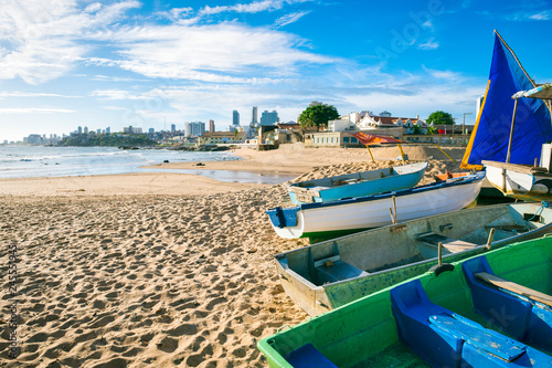 Traditional wooden boats painted in bright blues and greens line up on the shore of the fishing village of Rio Vermelho, in Salvador, Bahia, Brazil photo