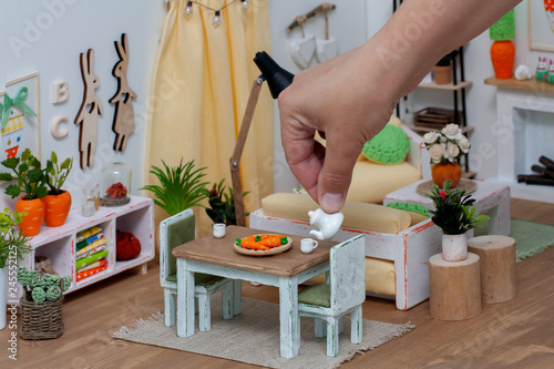 A cheerful bright room in a doll house furnished with miniature furniture, A person serving tea from a teapot for a play