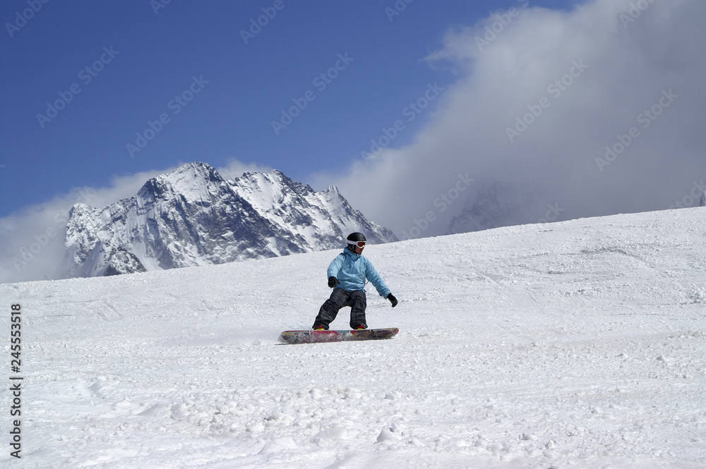 Snowboarder downhill on ski slope in high snowy mountains