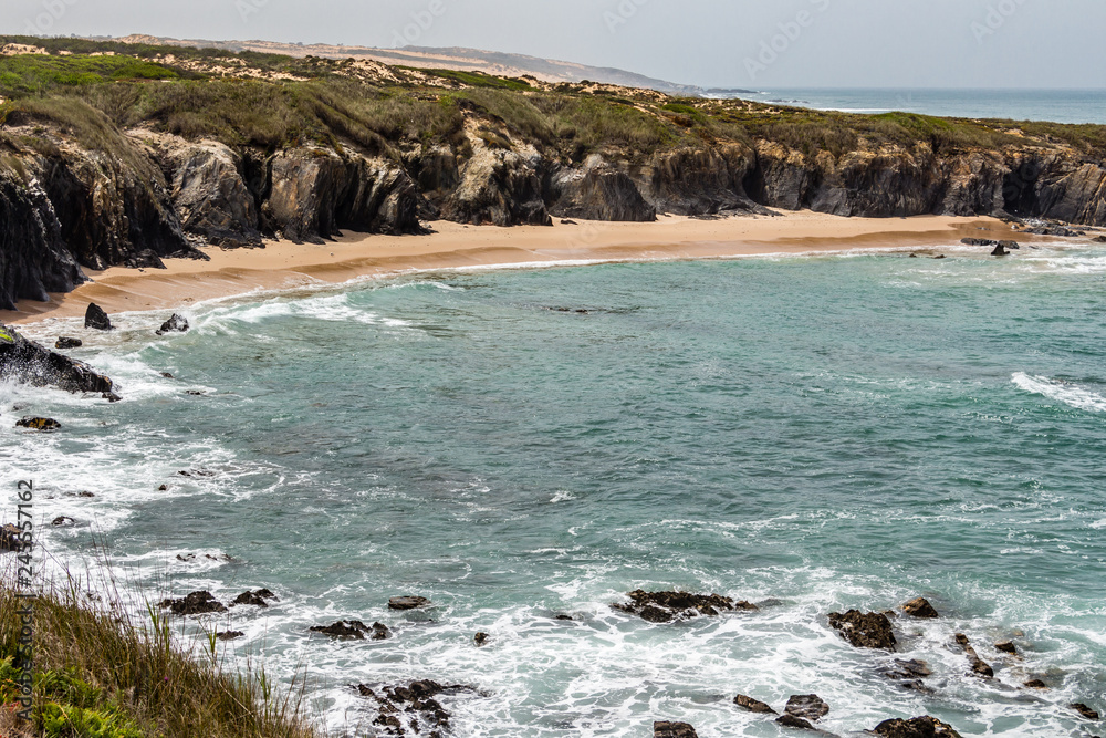 Obraz premium Wild sandy beach with cliffs on Atlantic ocean coast, Atlantic Ocean, Rota Vicentina, Alentejo, Portugal. Small waves hitting the rocks.