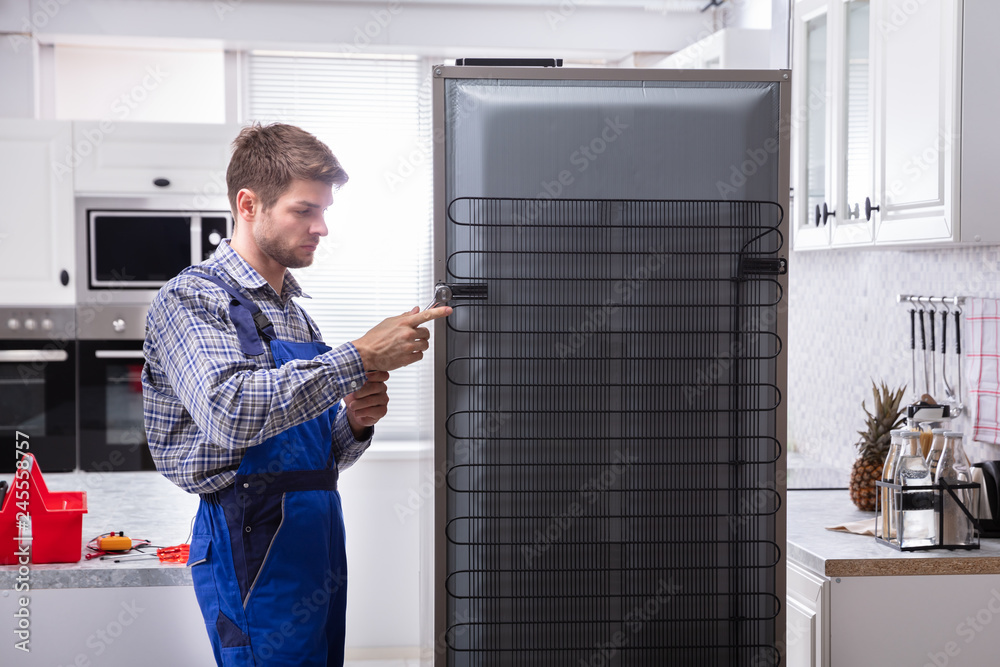 Serviceman In Overall Working On Fridge