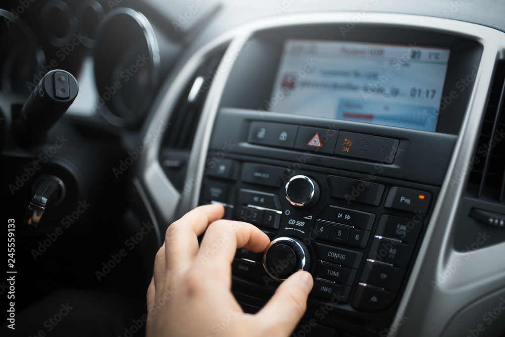 Close-up of man hand adjusts the volume control of car audio system.