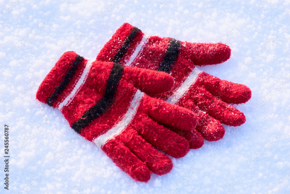 Red winter wool gloves are lying on pure white snow. texture. wallpaper. background. winter holiday concept