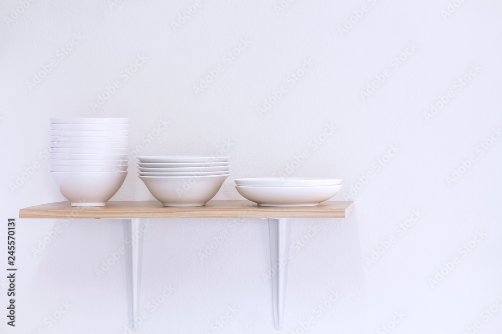 Wooden shelf template isolated on white wall background which on set stacked white bowls and plates as items tableware for decorated interior or montage of your product on shelf with copy space. Wooden shelf template isolated on white wall background which on set stacked white bowls and plates as items tableware for decorated interior or montage of your product on shelf with copy space.