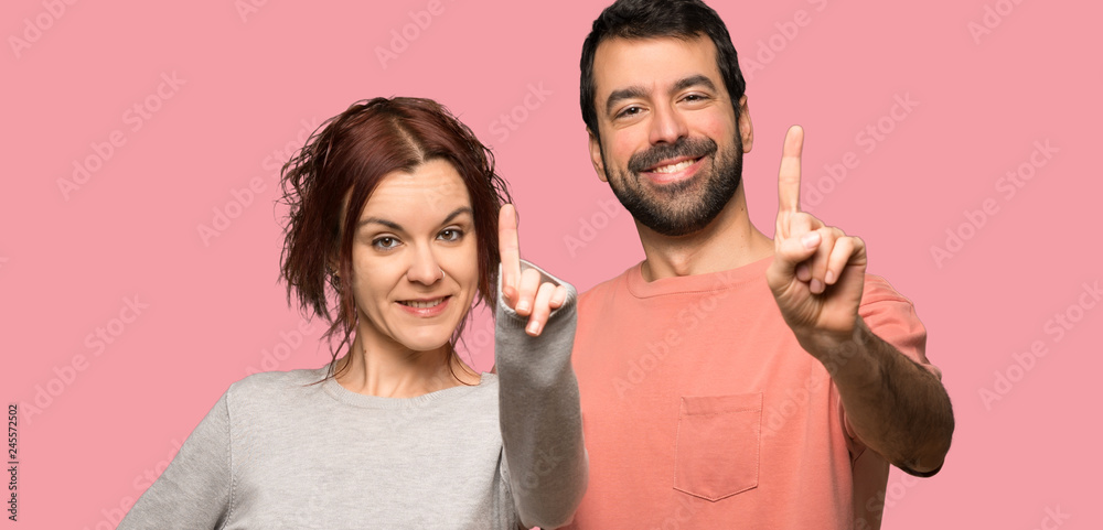 Fototapeta premium Couple in valentine day showing and lifting a finger over isolated pink background