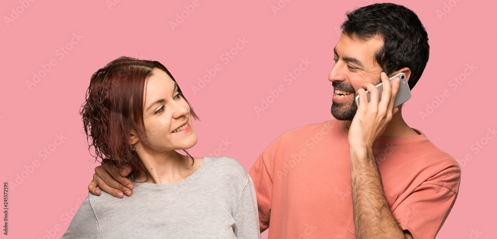 Couple in valentine day keeping a conversation with the mobile phone over isolated pink background Couple in valentine day keeping a conversation with the mobile phone over isolated pink background