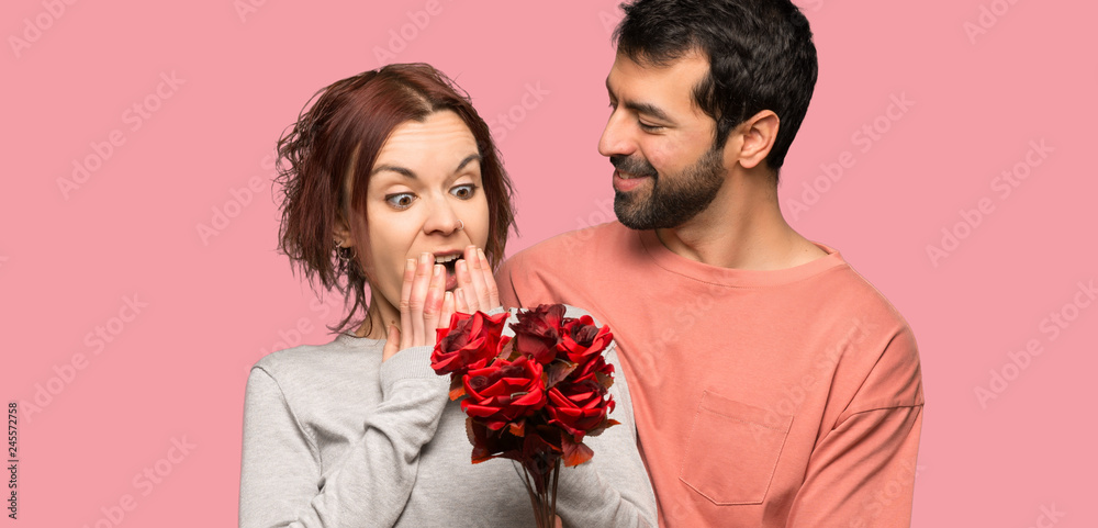 Couple in valentine day with flowers over isolated pink background Couple in valentine day with flowers over isolated pink background