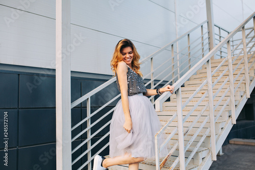 Attractive blonde girl in tulle skirt having fun on stairs. She is smiling down