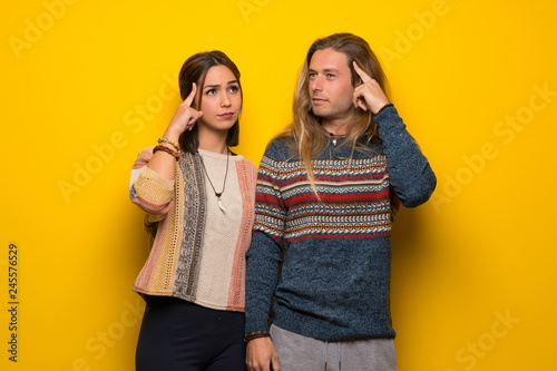 Hippie couple over yellow background having doubts and thinking