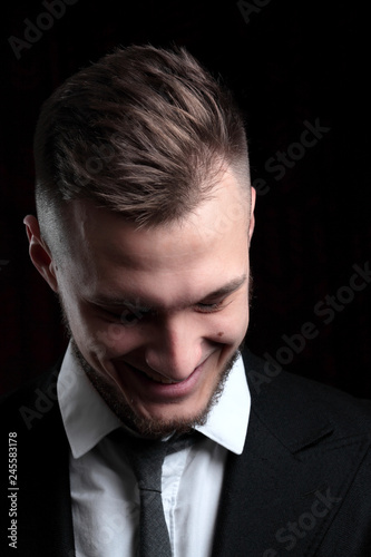 Close up portrait of elegant young fashion man in tuxedo laughing.on black background