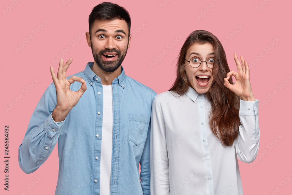 Alright gesture. Positive young woman and man make okay sign, recommend something of good quality, wear casual clothes, isolated over pink background. Recommendation and body language concept Alright gesture. Positive young woman and man make okay sign, recommend something of good quality, wear casual clothes, isolated over pink background. Recommendation and body language concept
