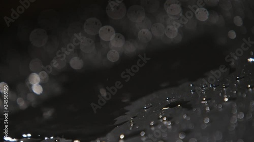 Drops of rainy water covering dark surface with spotty shadows in slow motion  