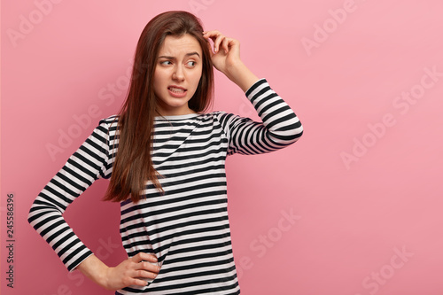 Foto Indoor shot of pretty woman scratches head, daydreams about something, tries mak