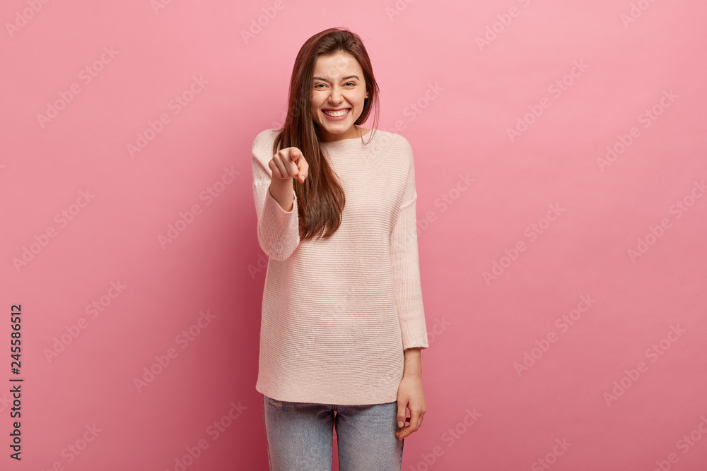 Horizontal shot of beautiful woman with satisfied expression, points directly at camera with fore finger, wears casual clothes, isolated over pink background, demonstrates her choice, chooses you Horizontal shot of beautiful woman with satisfied expression, points directly at camera with fore finger, wears casual clothes, isolated over pink background, demonstrates her choice, chooses you