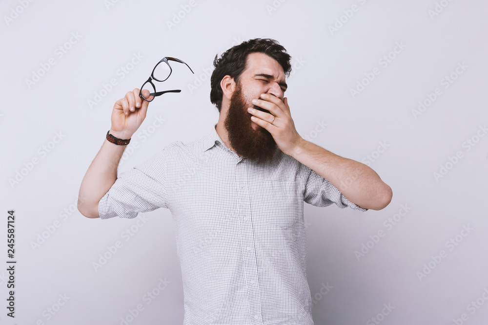 Handsome bearded man tired sleepy, yawning and covering mouth with hand