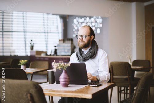 Freelance concept. Young bearded man using laptop while sitting in a  small cafe