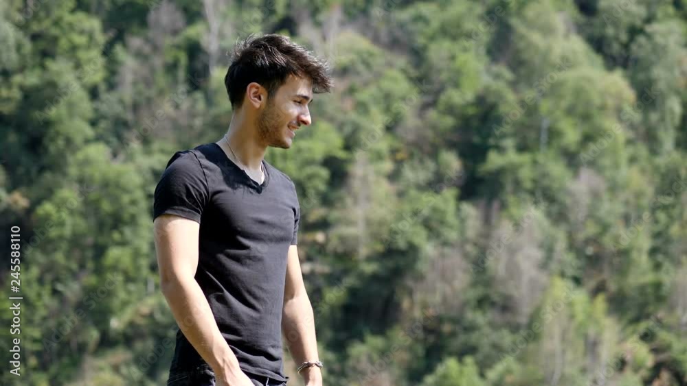 Handsome yung man standing on background of woods looking at camera then laughing with happiness Handsome yung man standing on background of woods looking at camera then laughing with happiness