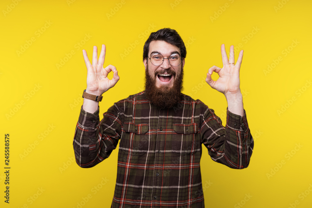 Fototapeta premium Handsome bearded man in round glasses and shirt is gesturing okay, like symbol