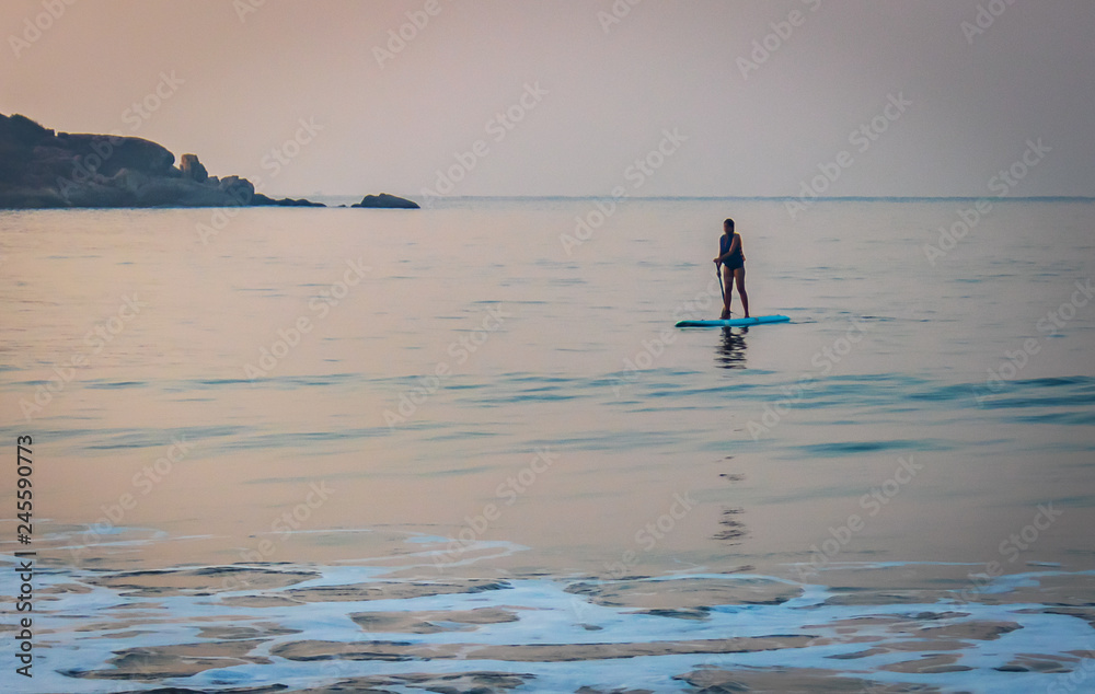 Stand up paddle boarding on a quiet sea with warm summer sunrise colors in south Goa palolem beach