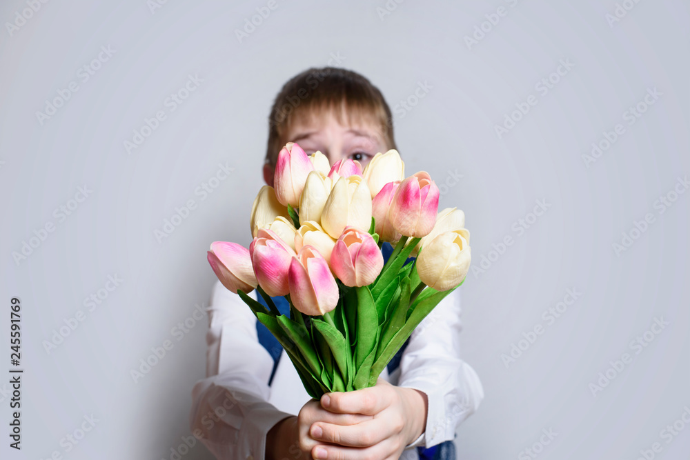 Little boy in white shirt gives a bouquet of tulips on light background. Little boy in white shirt gives a bouquet of tulips on light background.