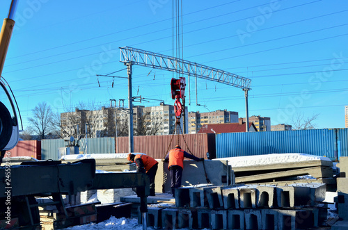 Workers are helping mobile crane to manage concrete joist. Mobile crane lifling truck with concrete slabs on construction site photo