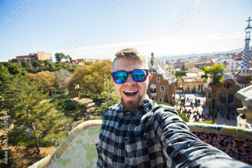 Travel and holidays concept - Happy guy making selfie portrait with smartphone in Park Guell, Barcelona, Spain.