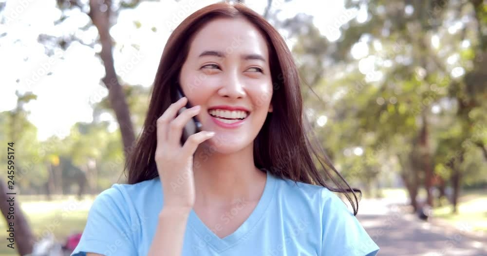 Beautiful young Asian woman using smartphone at park. Woman using smartphone with tree an natural in the background. Beautiful young Asian woman using smartphone at park. Woman using smartphone with tree an natural in the background.