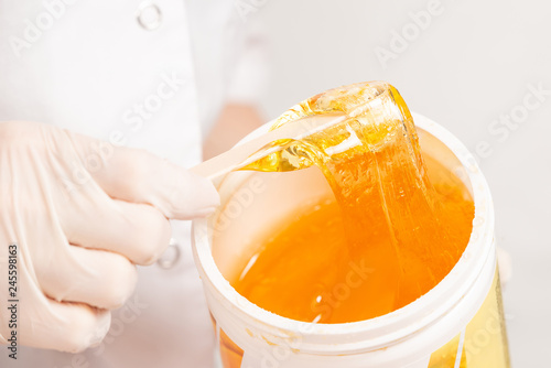 master of depilation in white latex gloves pulls out a wooden stick sugar paste from the jar