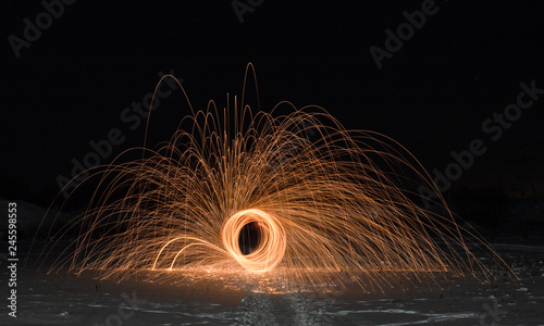 Light painting art. Spinning steel wool in abstract circle, firework showers of bright yellow glowing sparkles on winter snowy valley.