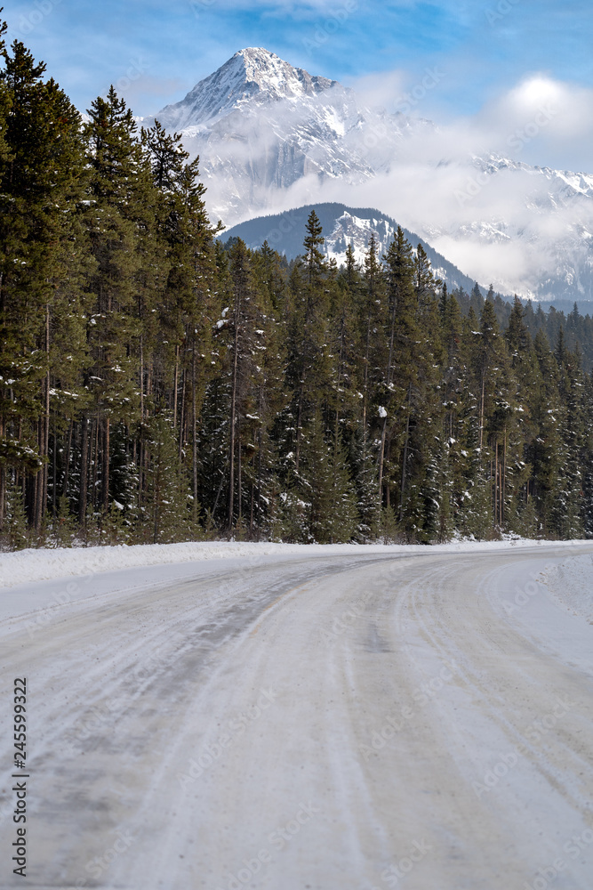 Bow Valley Parkway road covered in ice and snow with Cascade Mountain in background during winter in Banff National Park