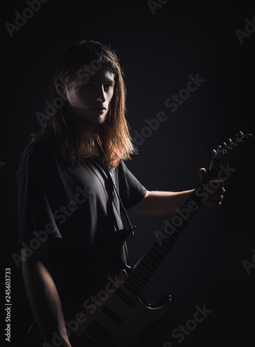 Dramatic studio portrait: handsome long-haired young man (rock musician) holds electric guitar in hands