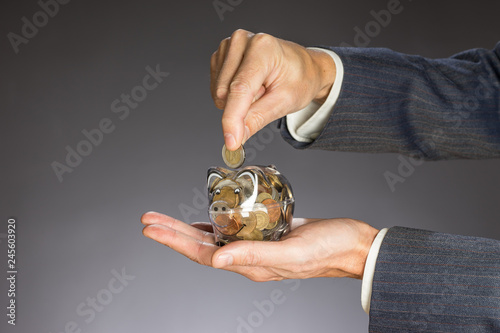 Business man with gray jacket putting euro coin  into the  piggi bank. European finance currency. Guy holding money box photo