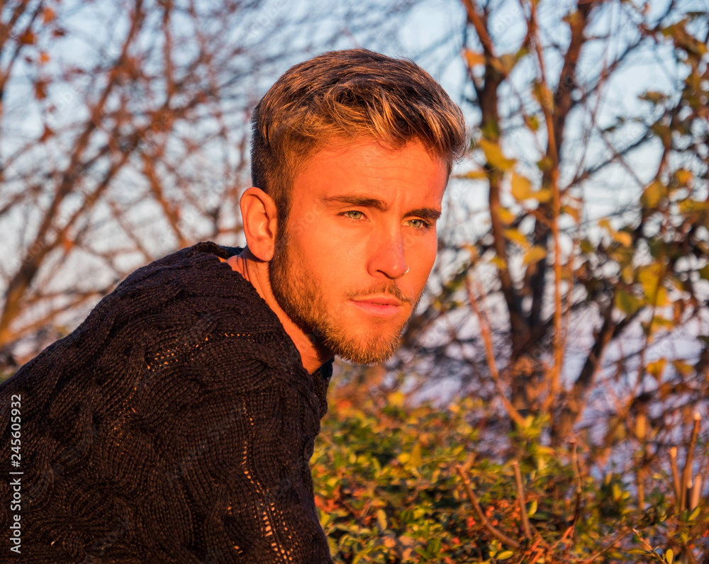 Handsome young man outdoor in winter fashion, wearing black coat and woolen scarf in city park
