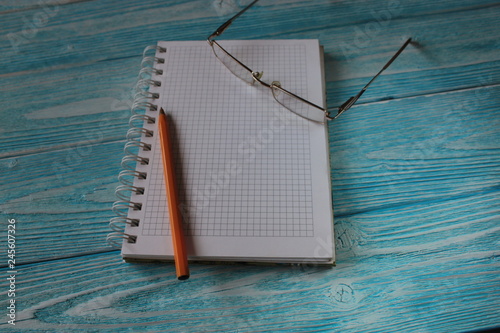 Блокнот , ручка  и очки лежат на синем деревянном столе. 
