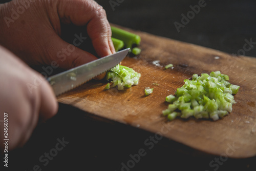 Woman preparing food in her kitchen, she is chopping fresh celery on a cutting board with a knife on the tray