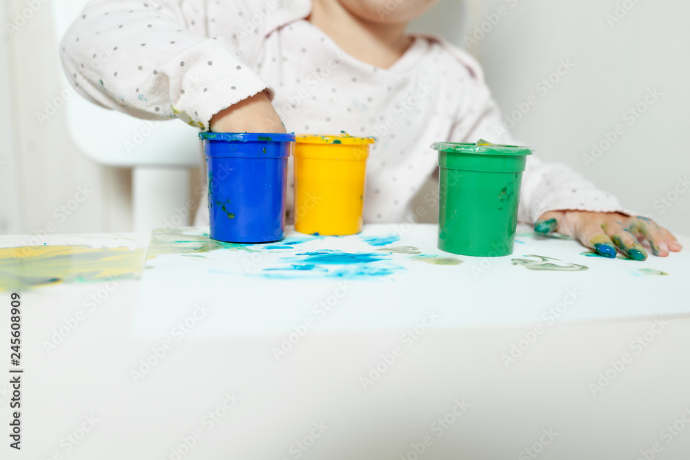Beautiful little girl draws with finger paints on a white sheet of paper. Creative child development in kindergarten or free time at home Beautiful little girl draws with finger paints on a white sheet of paper. Creative child development in kindergarten or free time at home