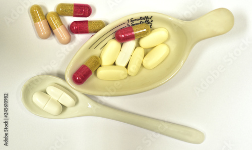 tabletten in tablettenschälchen und löffel vor weißem hintergrund