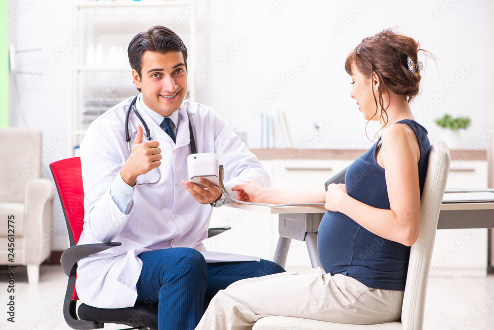 Fototapeta premium Young doctor checking pregnant woman's blood pressure
