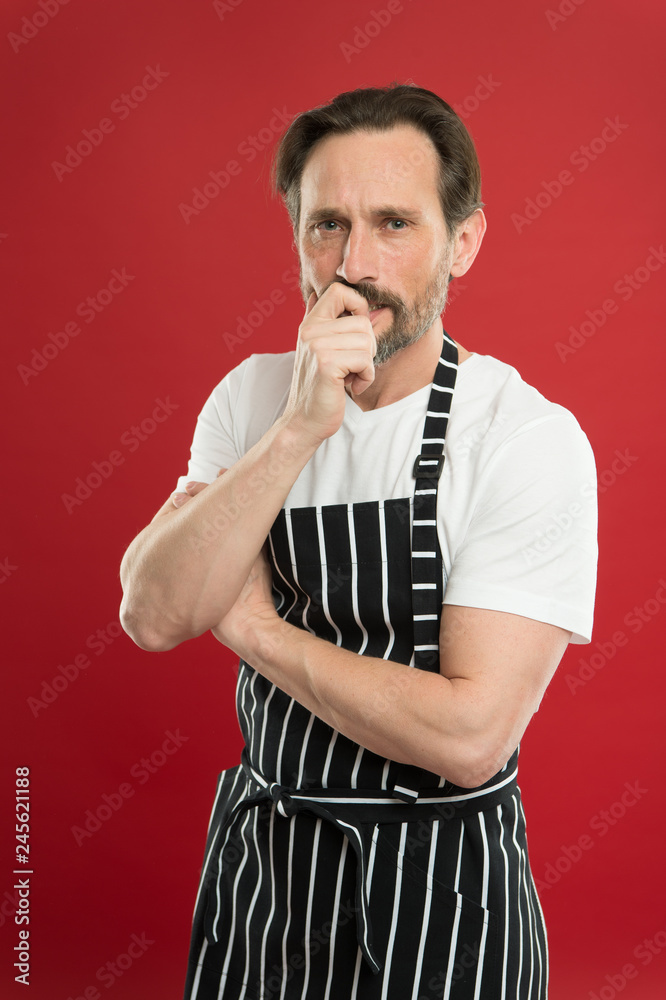 Concentrated on the task. Doing household. Bearded mature man in striped apron. Senior cook wearing bib apron. Mature person in cooking apron. Aged master of the household. Home cooking