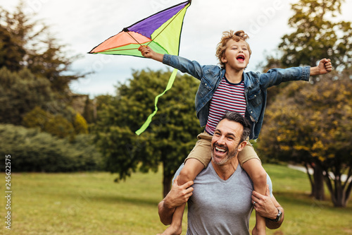 Smiling boy on fathers shoulders playing with kite photo