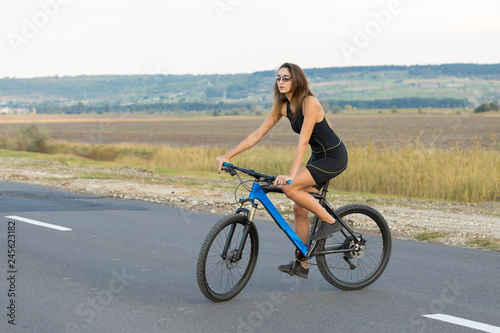 A girl riding a mountain bike on an asphalt road, beautiful portrait of a cyclist at sunset 