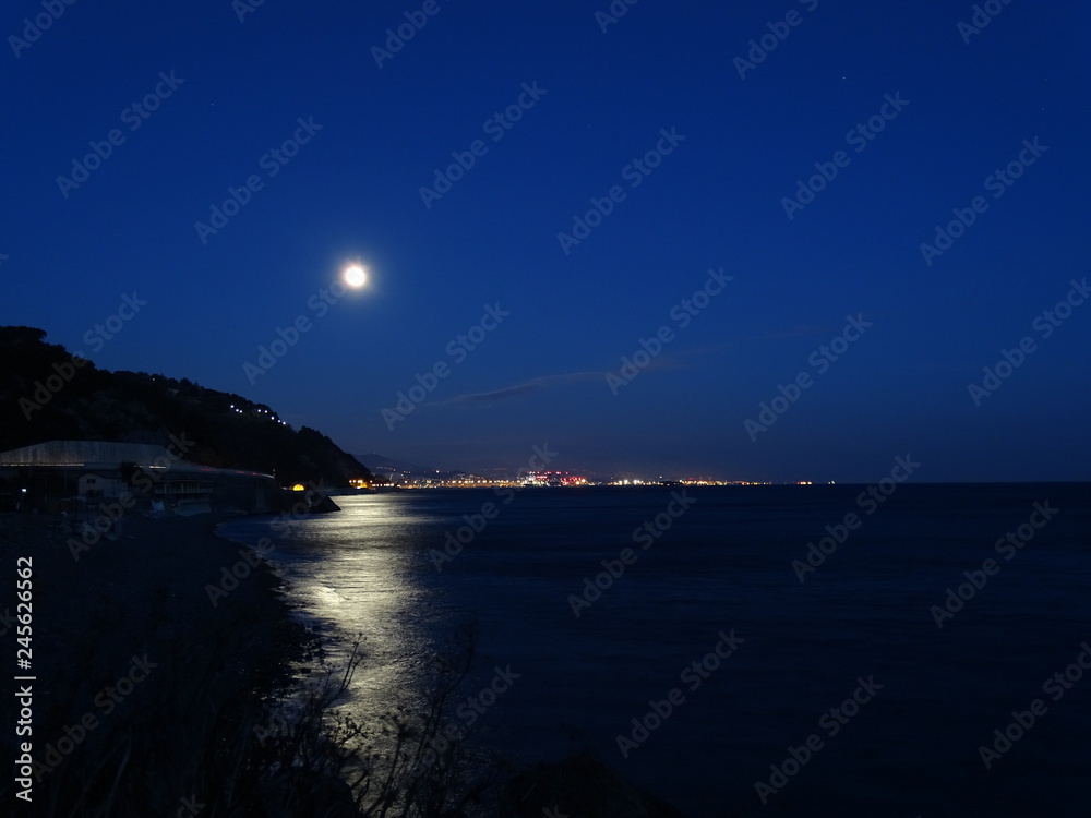 Fototapeta premium luna piena che si specchia nel mare sopra le luci del porto
