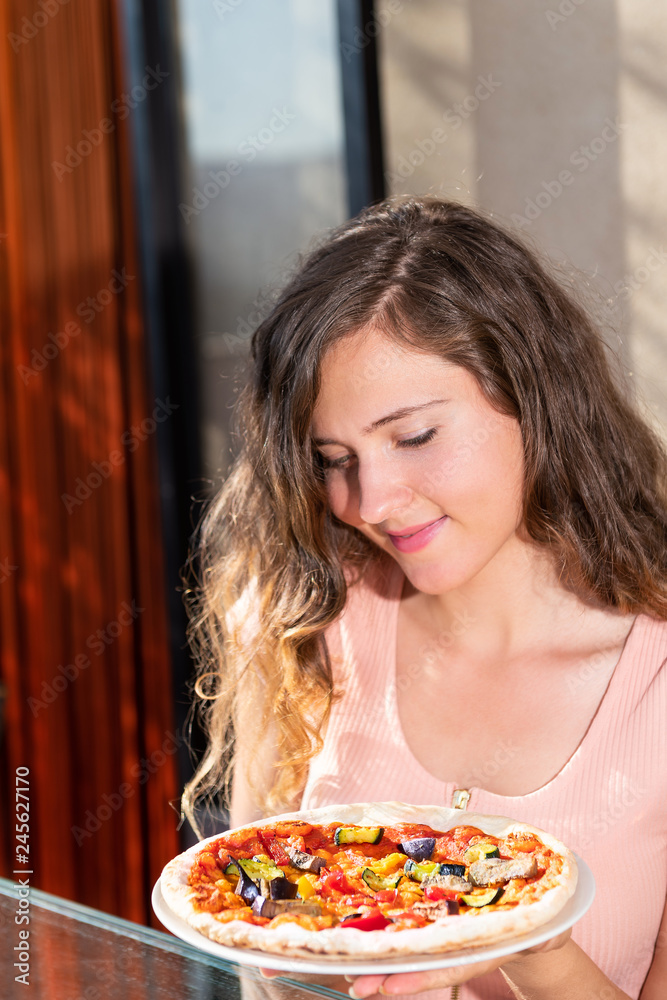 Young happy woman holding looking at whole small pizza on outside terrace patio in Italy vertical closeup portrait on vacation