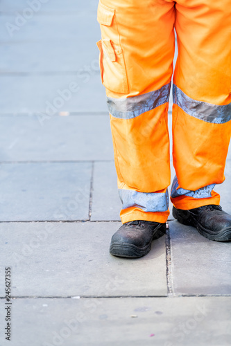Man worker cleaner construction site in orange uniform closeup legs on street in London road pavement during day