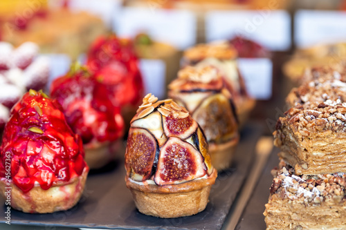 Fototapeta Naklejka Na Ścianę i Meble -  Display of many tarts cupcakes stuffed with cream desserts on trays in gourmet bakery cafe pastries closeup with fruit figs and strawberries